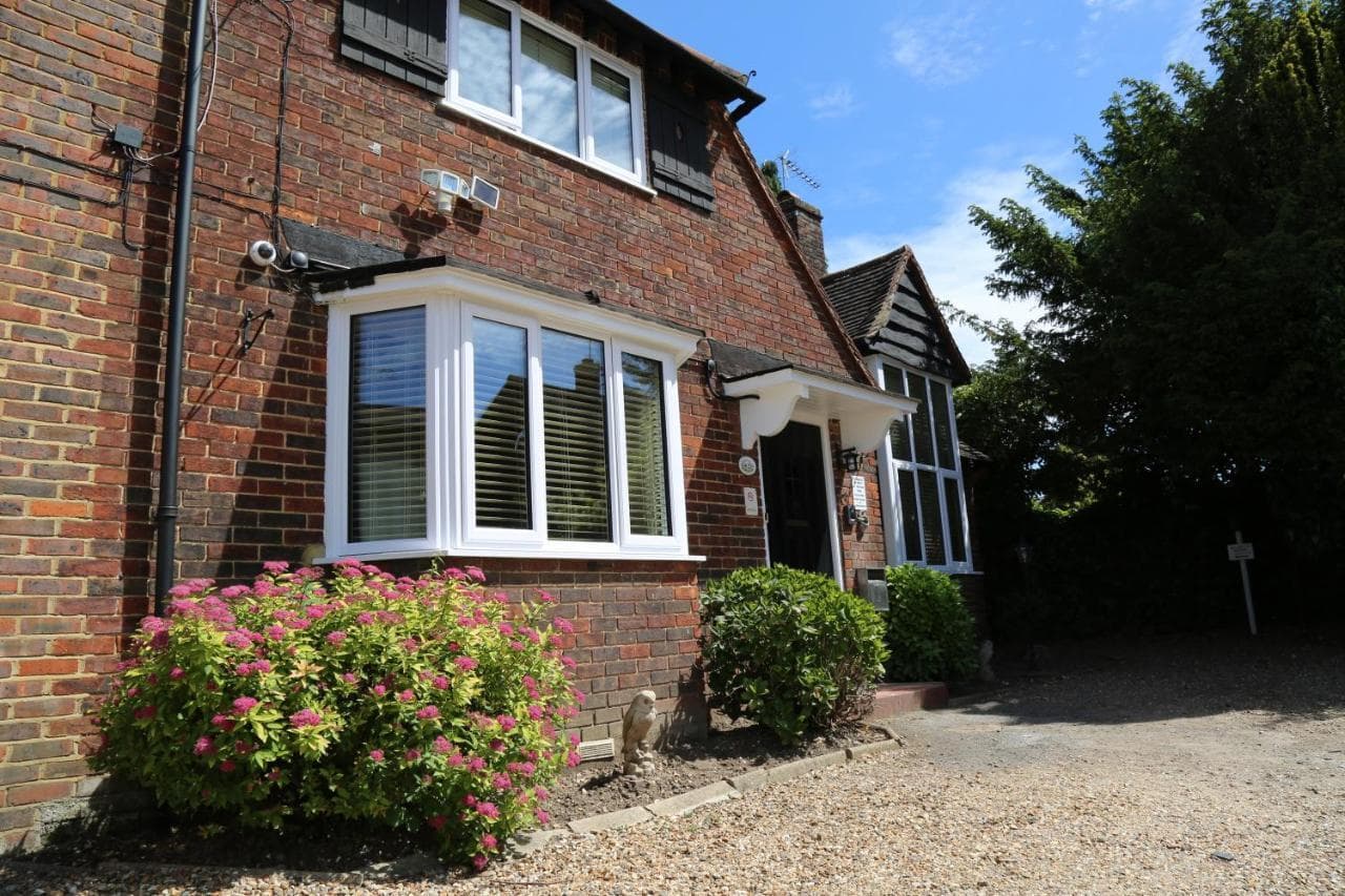 Debden Guest House: a red-brick house with white bay windows, a black front door and flowering shrubs