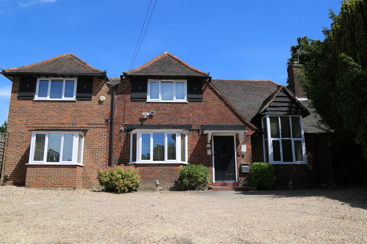 The front of Debden Guest House under a blue sky, with its gravel drive and parking