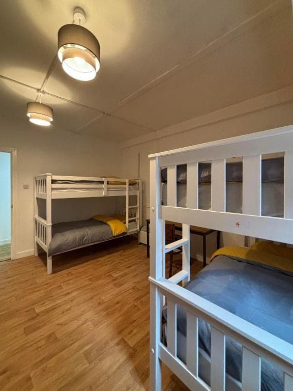 Six-bed dormitory with white bunk beds and wooden floor