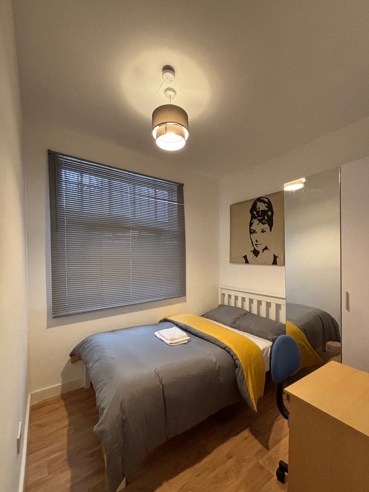 Double room at Sterling Suites Ealing with a grey and yellow bedspread, a framed print and a window with blinds